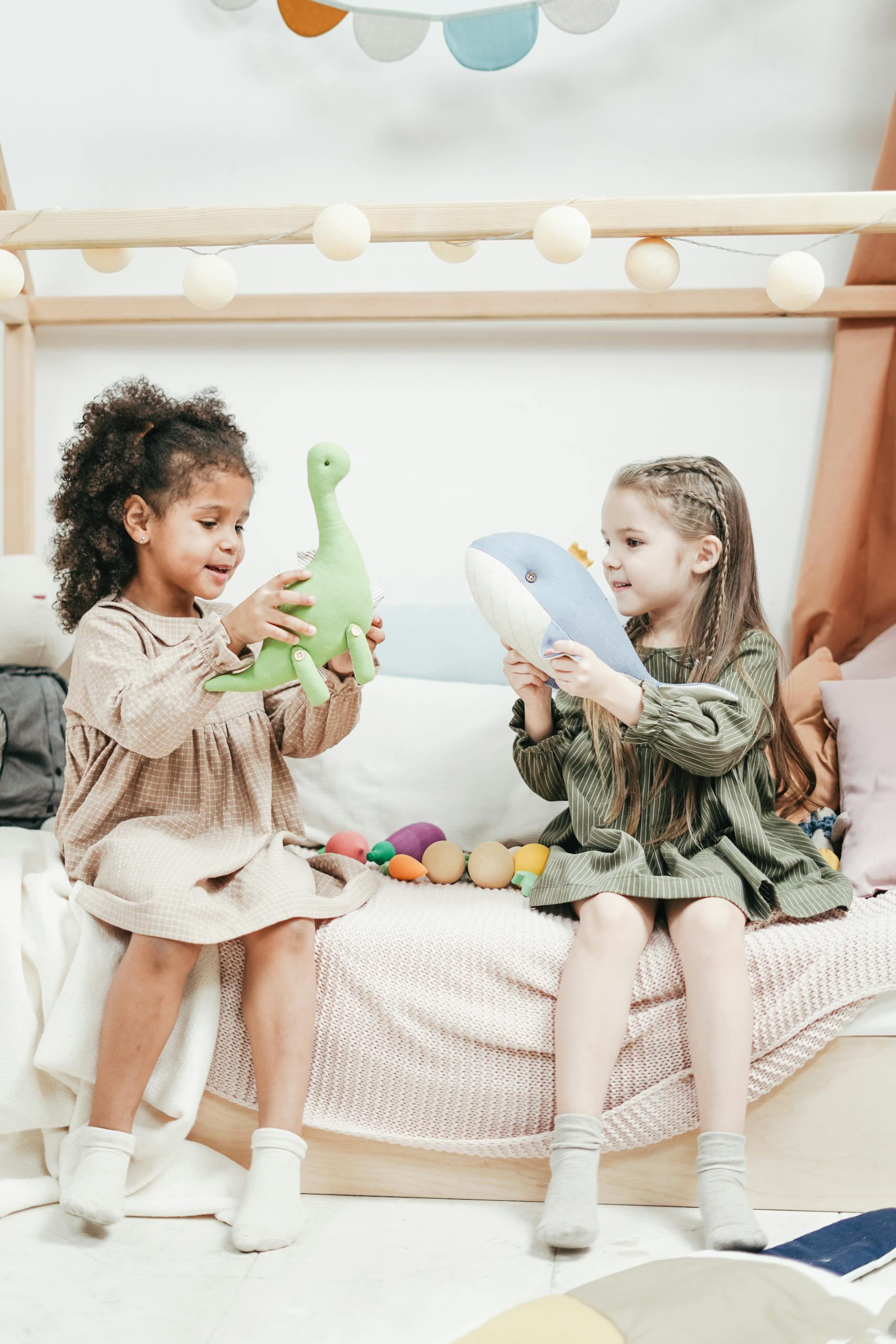 Two young girls playing happily with stuffed toys indoors in a cozy setting.